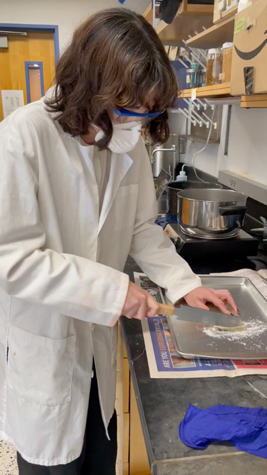 A person in a lab coat cutting something on a tray