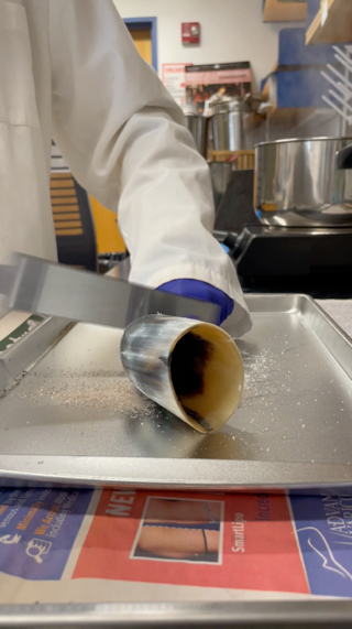 A person holding a knife over a metal container