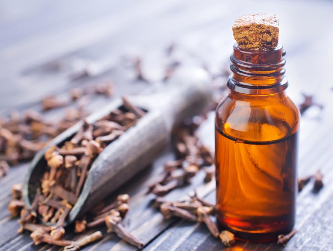 Scooper filled with dried clove next to brown glass vial